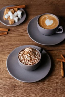 Kremalı kahve fincanları ve ahşap arka planda şeker dilimleri.