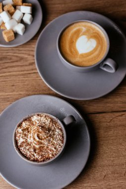 Kremalı kahve fincanları ve ahşap arka planda şeker dilimleri.