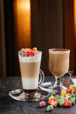 Kahve fincanlarında çikolata tozu ve masa arkasında karamelli likör şişesi olan renkli şekerler.