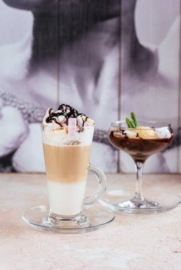 Krem şantili latte ve vanilyalı dondurma ile çikolatalı likör bardağı ve kırsal masa üzerinde renkli marşmelov.