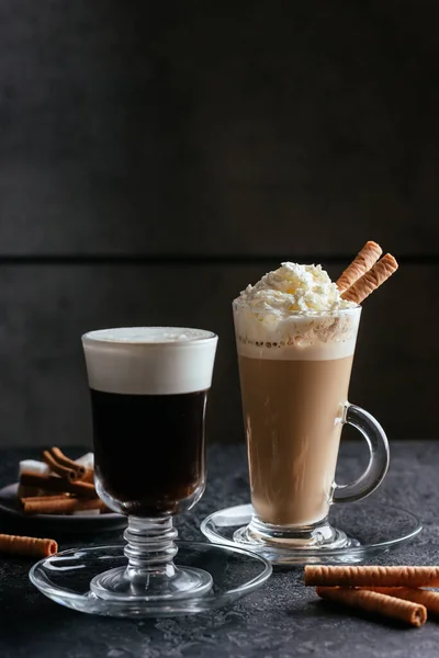 black coffee glass cup and cappuccino with whipped cream and sweet sticks on rustic table background