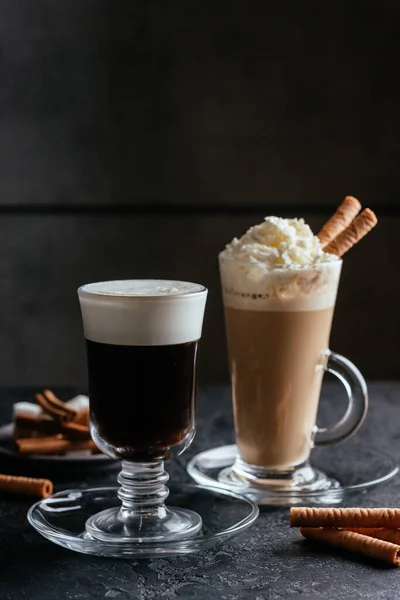 black coffee glass cup and cappuccino with whipped cream and sweet sticks on rustic table background