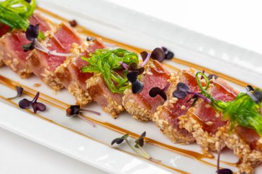 Baharatlı susamlı et, otlar, yeşiller ve beyaz tabakta sos. 