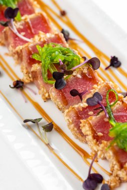 Baharatlı susamlı et, otlar, yeşiller ve beyaz tabakta sos. 