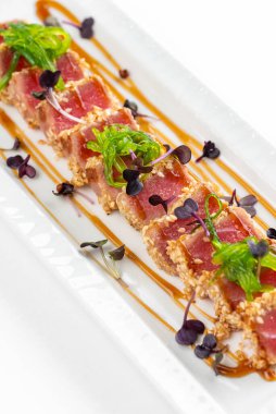 Baharatlı susamlı et, otlar, yeşiller ve beyaz tabakta sos. 