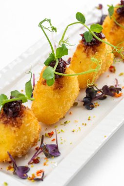 Üzümlü kızarmış Camembert dilimleri, ahududu sosu ve beyaz tabakta yeşillikler.