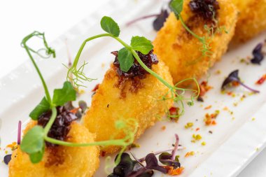 Üzümlü kızarmış Camembert dilimleri, ahududu sosu ve beyaz tabakta yeşillikler.