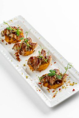 Patatesli kanepe dilimleri ızgara füme yılan balığı ve beyaz tabakta sos.