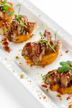 Patatesli kanepe dilimleri ızgara füme yılan balığı ve beyaz tabakta sos.