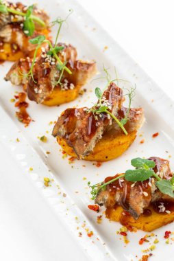 Patatesli kanepe dilimleri ızgara füme yılan balığı ve beyaz tabakta sos.