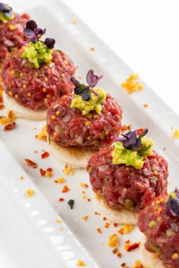 Beyaz ekmek dilimleri ve avokado makarnalı biftek tartar kanepesi.