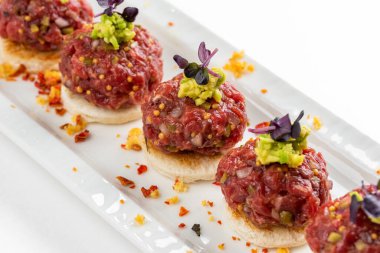 Beyaz ekmek dilimleri ve avokado makarnalı biftek tartar kanepesi.