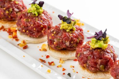 Beyaz ekmek dilimleri ve avokado makarnalı biftek tartar kanepesi.