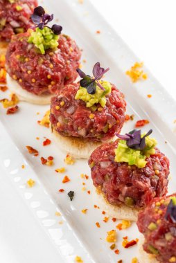 Beyaz ekmek dilimleri ve avokado makarnalı biftek tartar kanepesi.