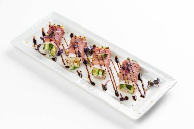 Parma jambonlu kanepe, yeşil salatalıklı ve beyaz tabakta kahverengi soslu.  