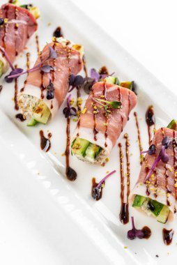 Parma jambonlu kanepe, yeşil salatalıklı ve beyaz tabakta kahverengi soslu.  