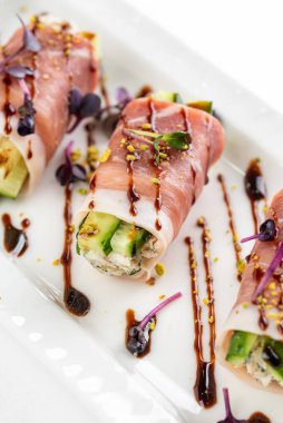 Parma jambonlu kanepe, yeşil salatalıklı ve beyaz tabakta kahverengi soslu.  