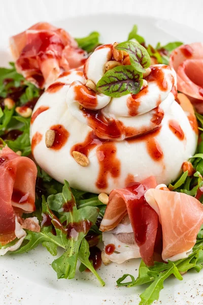 İtalyan şarküteri salatası, burrata peyniri ve beyaz tabakta parma jambonu dilimleri. 