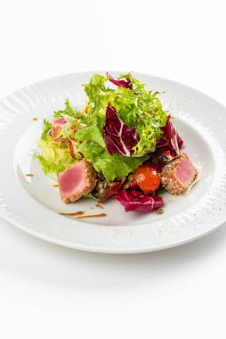 Lezzetli ton balığı dilimleri, yeşiller ve domatesli beyaz tabakta salata