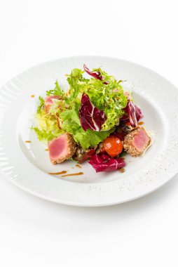 Lezzetli ton balığı dilimleri, yeşiller ve domatesli beyaz tabakta salata