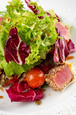 Lezzetli ton balığı dilimleri, yeşiller ve domatesli beyaz tabakta salata