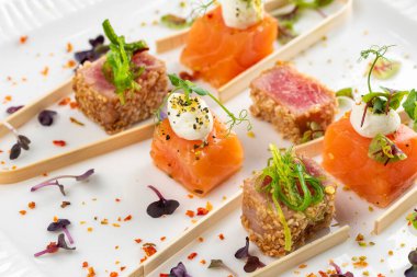 Somon ve ton balığı dilimlenmiş krem peynir ve beyaz tabakta yeşillikler.