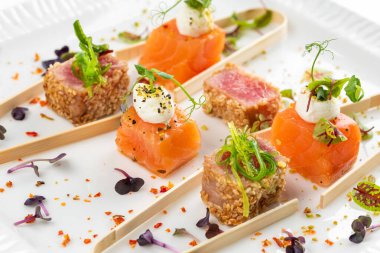 Somon ve ton balığı dilimlenmiş krem peynir ve beyaz tabakta yeşillikler.