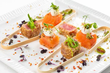 Somon ve ton balığı dilimlenmiş krem peynir ve beyaz tabakta yeşillikler.