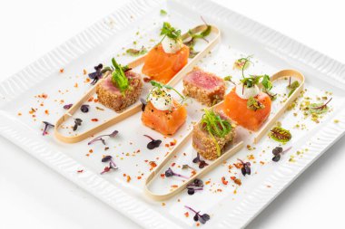 Somon ve ton balığı dilimlenmiş krem peynir ve beyaz tabakta yeşillikler.