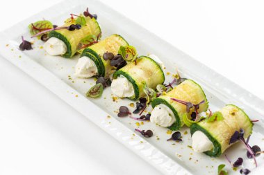 Kabak dürümleri, krem peynir ve yeşiller beyaz tabakta. 