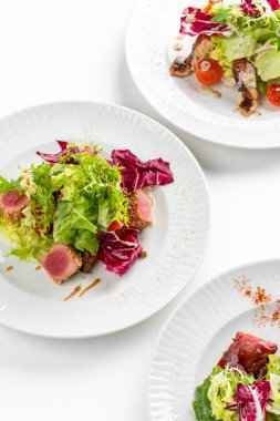 Beyaz masa arkasında ton balığı dilimleri, somon, yeşillik ve domatesli renkli salata tabakları.