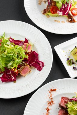 yeşil ve kırmızı salata tabakları ton balığı dilimleri, somon balığı ve domatesler gri masa arkasında