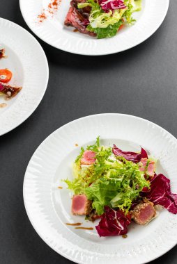 yeşil ve kırmızı salata tabakları ton balığı dilimleri, somon balığı ve domatesler gri masa arkasında