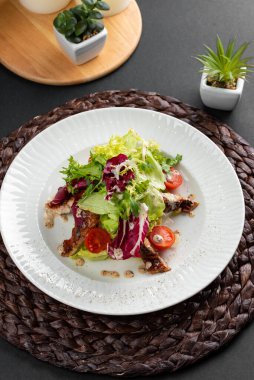 Renkli lezzetli salata, fırında somon, yeşillik ve domatesler kırsal ahşap peçetede beyaz tabakta. 