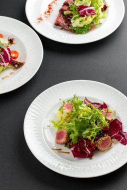 yeşil ve kırmızı salata tabakları ton balığı dilimleri, somon balığı ve domatesler gri masa arkasında
