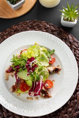 Renkli lezzetli salata, fırında somon, yeşillik ve domatesler kırsal ahşap peçetede beyaz tabakta. 