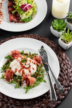 İtalyan şarküteri salatalı burrata peyniri. Parma jambonu dilimlenmiş. Köy peçetesinde çatal ve bıçakla. 