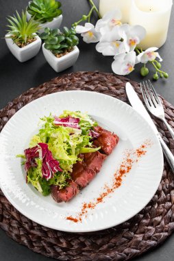 sığır eti dilimli renkli salata, yeşiller ve kırsal peçetede beyaz tabakta kırmızı biber.