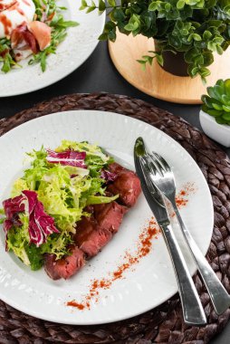 sığır eti dilimli renkli salata, yeşiller ve kırsal peçetede beyaz tabakta kırmızı biber.