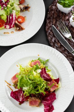 İtalyan yeşil ve kırmızı salata tabakları ton balığı dilimleri, somon balığı ve domatesler gri masa arkasında.