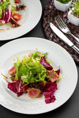 İtalyan yeşil ve kırmızı salata tabakları ton balığı dilimleri, somon balığı ve domatesler gri masa arkasında.