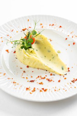 Domates dilimiyle süslenmiş tereyağlı patates püresi ve beyaz tabakta kırmızı biber. 