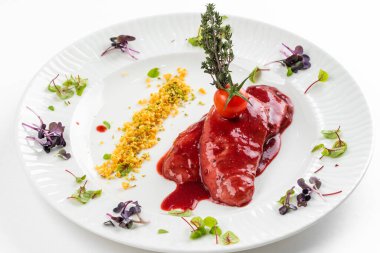 Kırmızı sosun altında kızarmış ördek filetosu ve beyaz tabakta domates. 