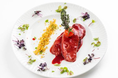 Kırmızı sosun altında kızarmış ördek filetosu ve beyaz tabakta domates. 