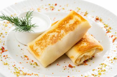 Lezzetli kızarmış Rus krepleri, altın hamurlu ve beyaz ekşi krema kasesi, kırsal masa arka planında.