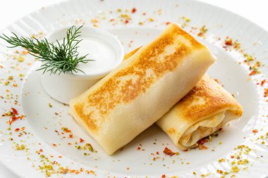 Lezzetli kızarmış Rus krepleri, altın hamurlu ve beyaz ekşi krema kasesi, kırsal masa arka planında.