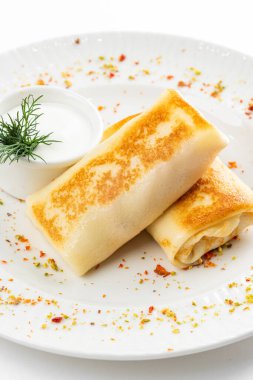 Lezzetli kızarmış Rus krepleri, altın hamurlu ve beyaz ekşi krema kasesi, kırsal masa arka planında.