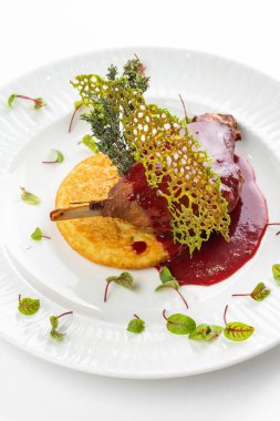 Beyaz tabakta kırmızı böğürtlen soslu patates pirzolası ile fırında ördek bacağı. 