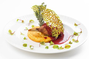 Beyaz tabakta kırmızı böğürtlen soslu patates pirzolası ile fırında ördek bacağı. 