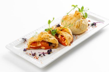 Domatesli fırınlanmış çörekler ve beyaz tabakta yeşillikle süslenmiş peynir. 